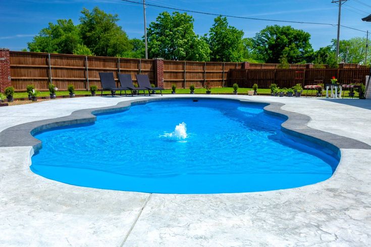 Fiberglass pool with a fountain feature, surrounded by a concrete patio and lounge chairs, set in a residential backyard in Hopewell Junction, NY, illustrating Coastal Pools and Spas' installation expertise.