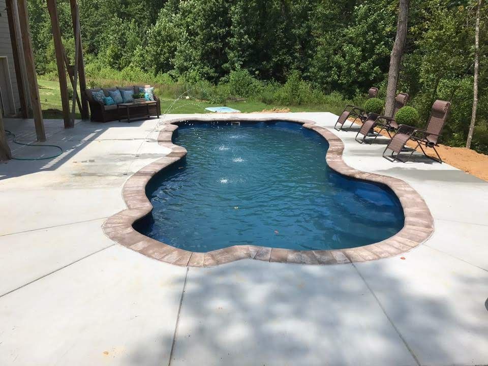 Fiberglass pool installation in a landscaped backyard with lounge chairs, showcasing clear water and surrounding greenery, emphasizing outdoor living and relaxation.