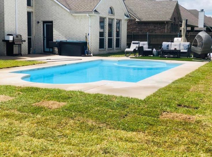 Fiberglass pool surrounded by manicured lawn and patio area with seating, showcasing a modern backyard design ideal for relaxation and entertainment.