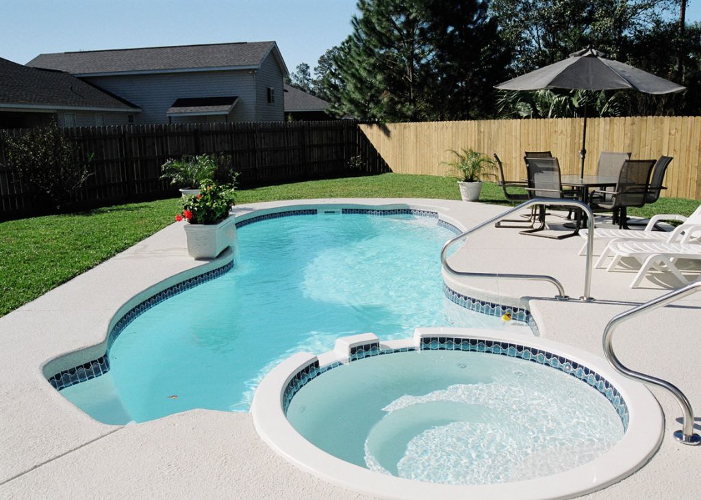Fiberglass pool with attached spa in a landscaped backyard, featuring a patio set and umbrella, showcasing Coastal Pools and Spas' custom design options for homeowners in Clinton Corners, NY.