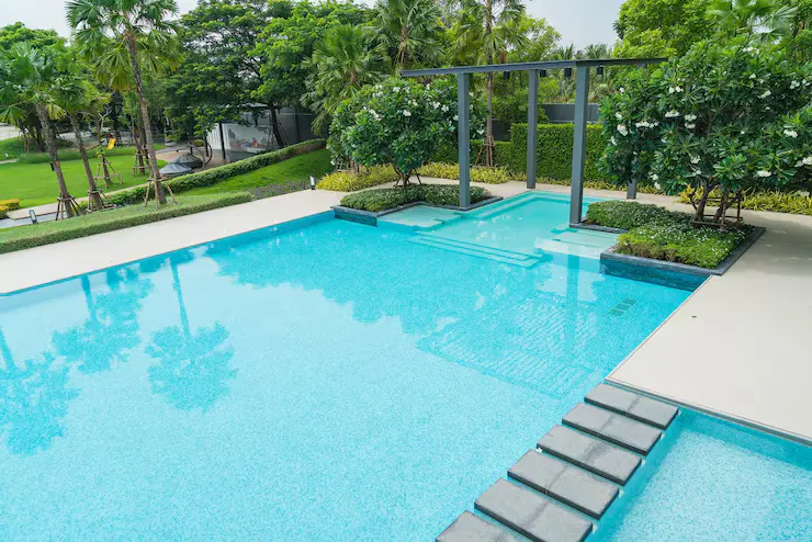 Luxury fiberglass swimming pool with a modern design, surrounded by lush greenery and palm trees, featuring a stylish deck and seating area, ideal for outdoor living and relaxation.