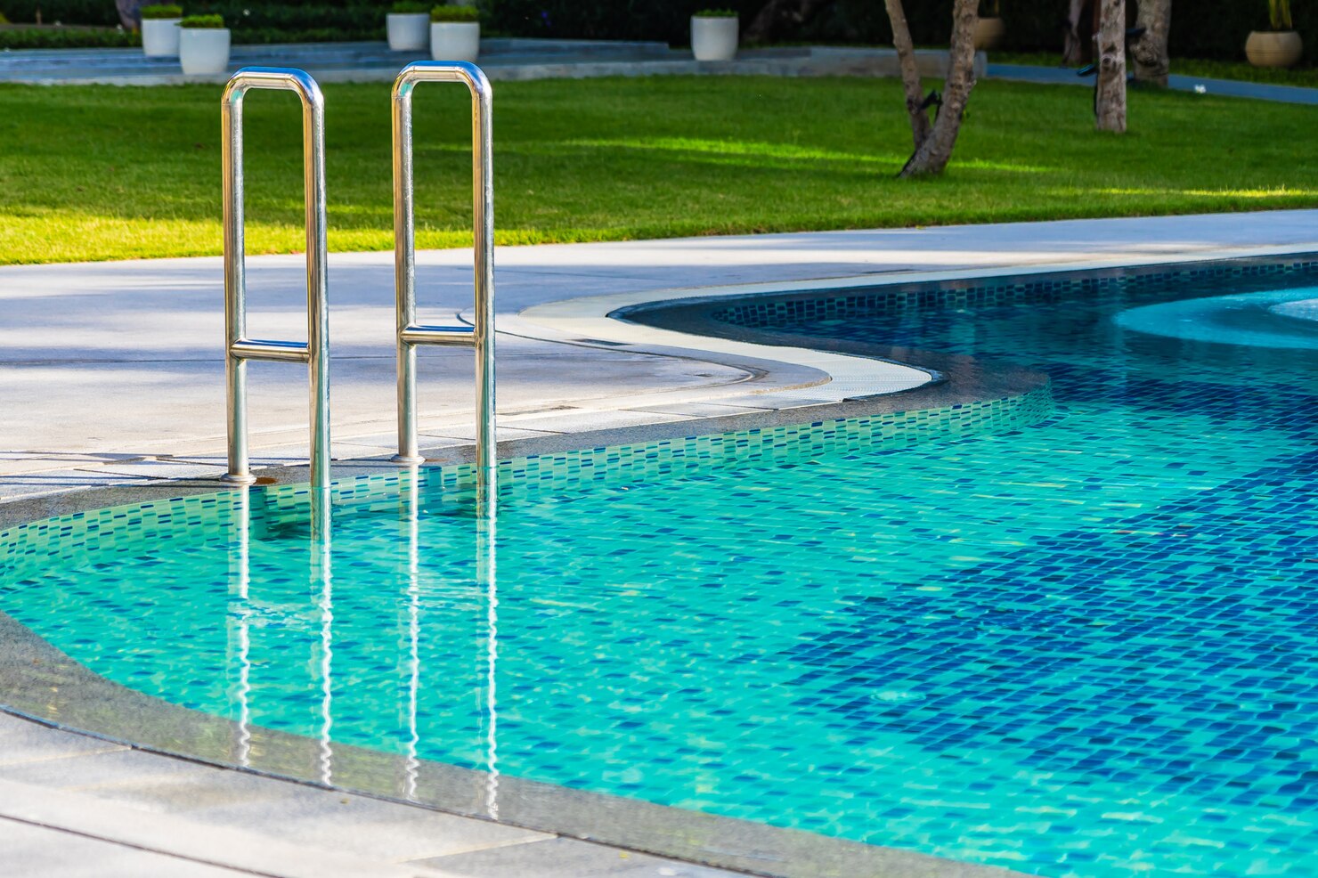 Swimming pool with stainless steel ladder and clear blue water, surrounded by landscaped grass and decorative planters, highlighting low-maintenance fiberglass pool features.