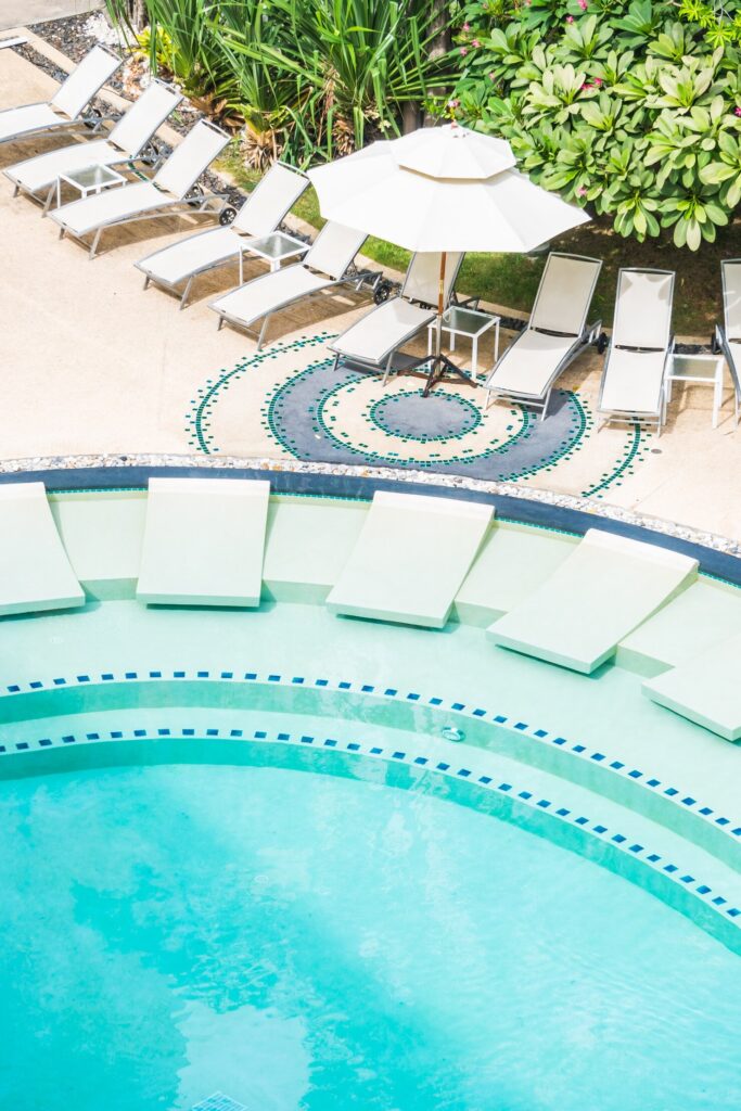 Circular fiberglass pool with turquoise water, surrounded by lounge chairs and an umbrella, showcasing a decorative tile pattern, emphasizing a relaxing outdoor space ideal for families in Waccabuc, NY.