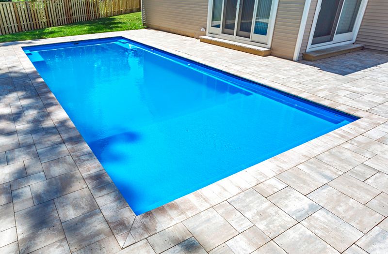 Fiberglass swimming pool installed in a residential backyard with stone patio, showcasing a clear blue water surface and adjacent home features in Hopewell Junction, NY.