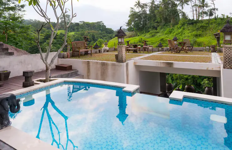 Hotel swimming pool with clear blue water, surrounded by a landscaped patio featuring seating areas, lanterns, and lush greenery, emphasizing outdoor living and relaxation spaces.