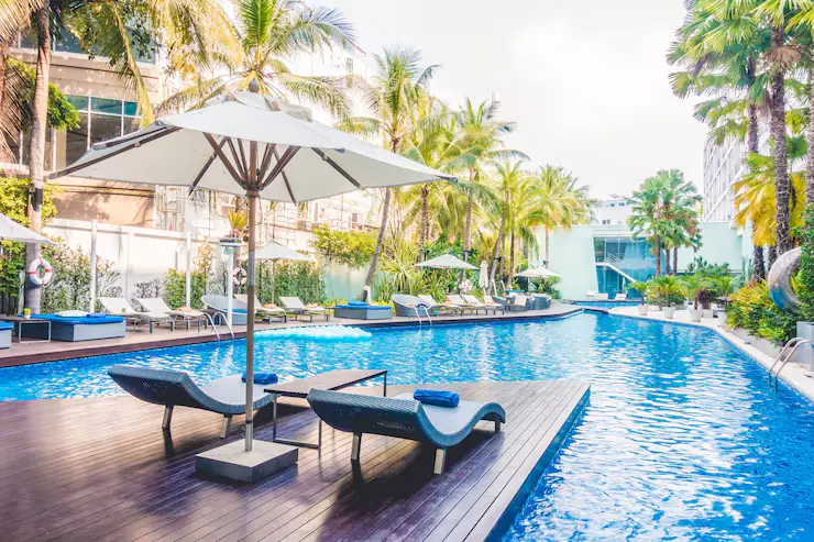 Modern fiberglass pool with lounge chairs and umbrellas surrounded by tropical palm trees, reflecting a serene backyard oasis ideal for family enjoyment in Mahopac, NY.
