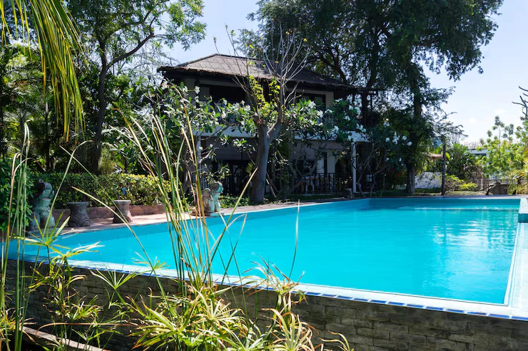 Fiberglass swimming pool with clear blue water surrounded by tropical plants and a garden, showcasing a residential backyard setting ideal for outdoor enjoyment.