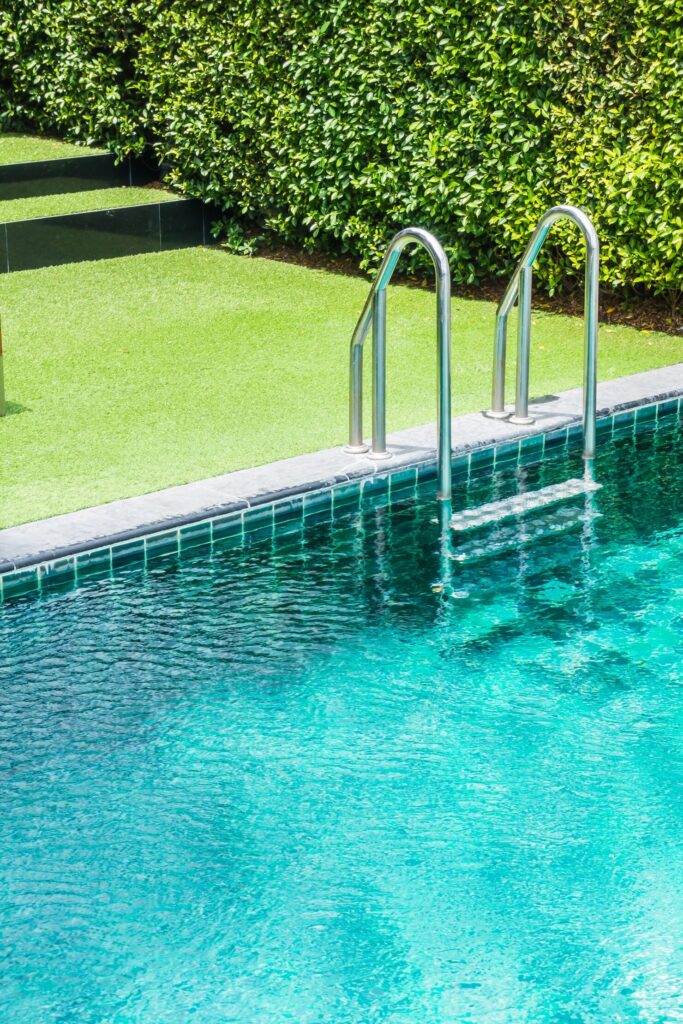 Swimming pool ladder beside clear blue water and lush green grass, illustrating a well-integrated backyard design for fiberglass pools in West Harrison, NY.