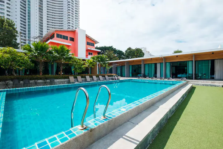 Modern swimming pool with clear blue water, surrounded by lush greenery and lounge chairs, featuring a contemporary building in the background, ideal for outdoor living and relaxation.