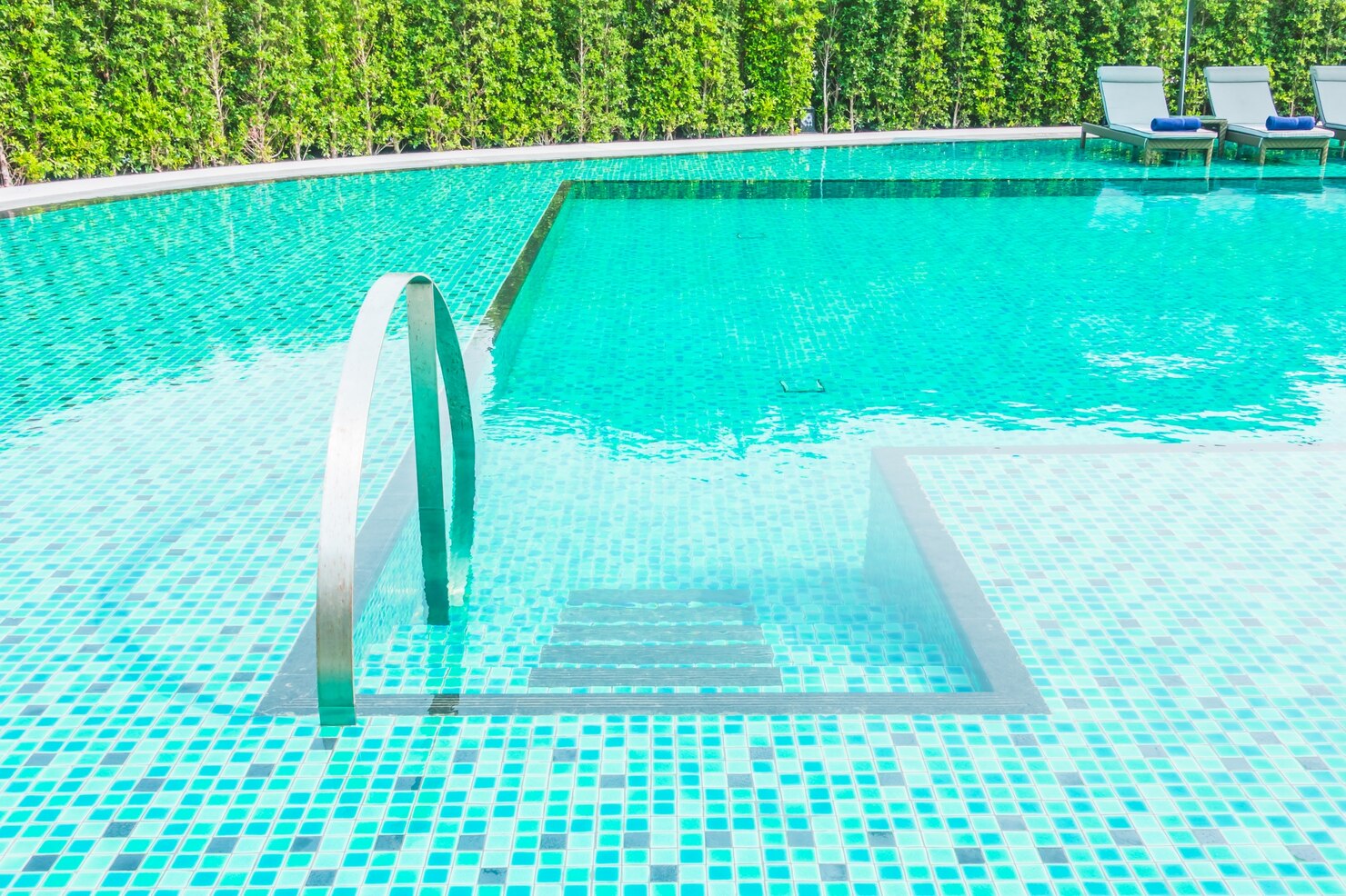 Fiberglass swimming pool with modern design, featuring a stainless steel ladder and turquoise mosaic tiles, surrounded by lush greenery and lounge chairs, reflecting Coastal Pools & Spas' expertise in custom pool installations in Chappaqua, NY.