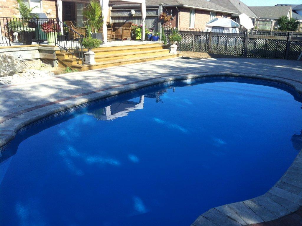 Fiberglass swimming pool with clear blue water, surrounded by patio and landscaping, showcasing residential backyard design for Coastal Pools & Spas in Verbank, NY.